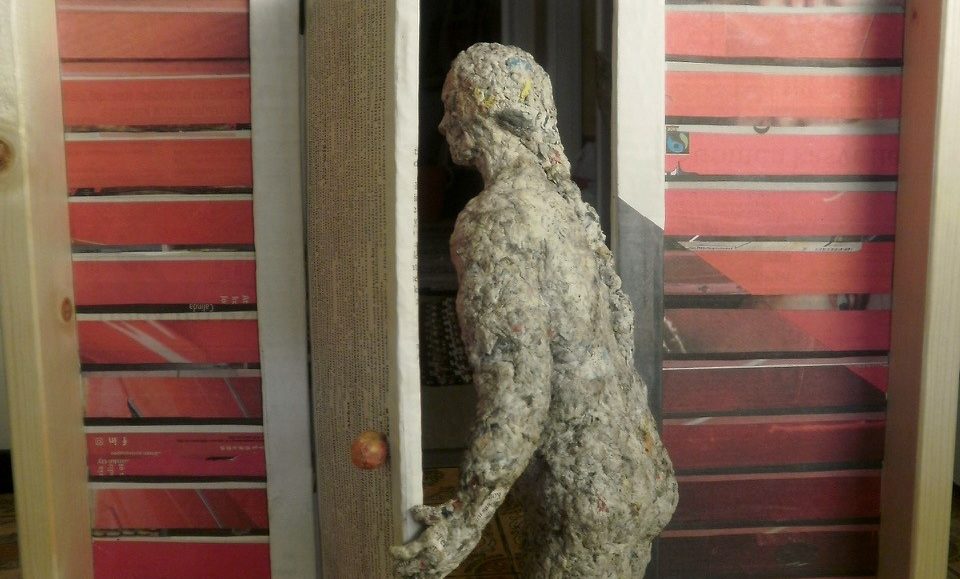 Potreteista paperitöihin näyttelyn työ, jossa naisfiguuri on astumassa ovesta sisään.